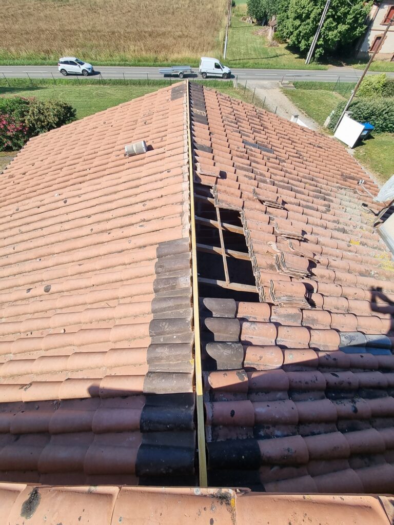 Toit en tuiles de terre cuite en cours de rénovation, une partie de la couverture est retirée révélant la charpente en bois.