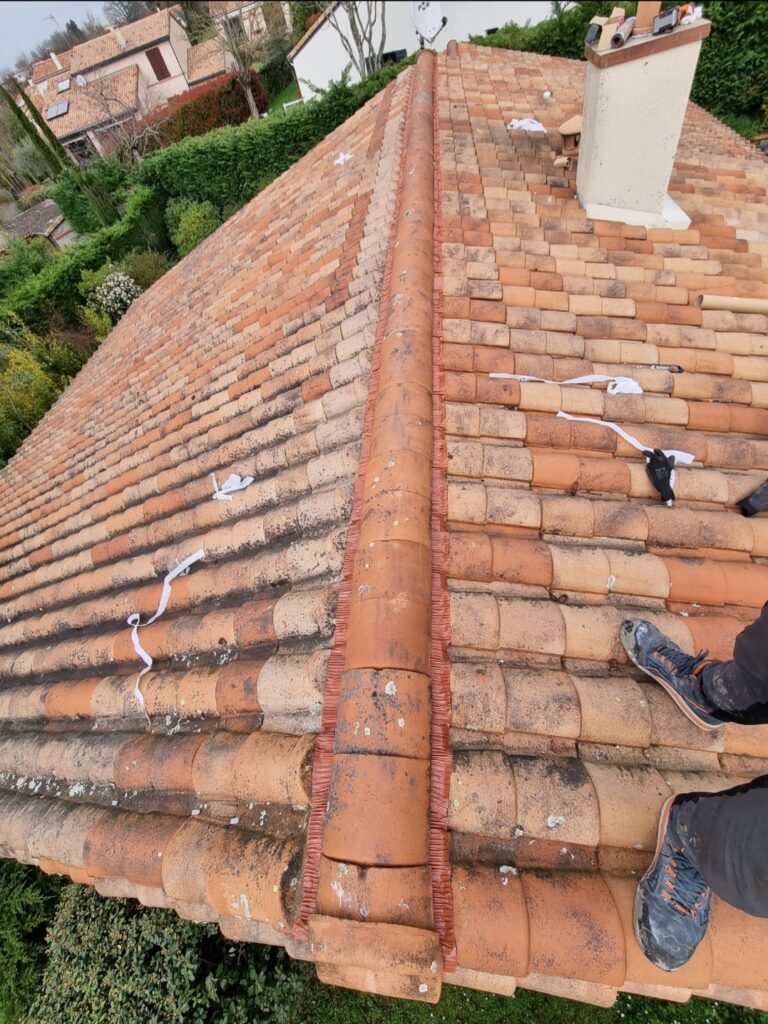 Rénovation de toit en tuiles romaines terre cuite, vue du dessus. Pose de faîtière avec bande ventilée. Un couvreur sur le versant droit.