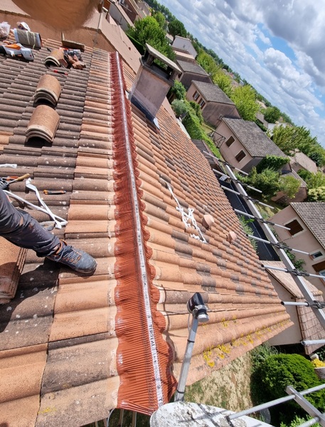 Rénovation de toiture en tuiles: un ouvrier installe un closoir de faîtage ventilé TERREAL pour l'étanchéité. Outils et tuiles prêts.